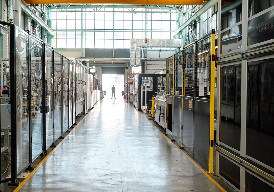 A figure stands in a loading door, we are watching them from the other side of the room past some other equipment