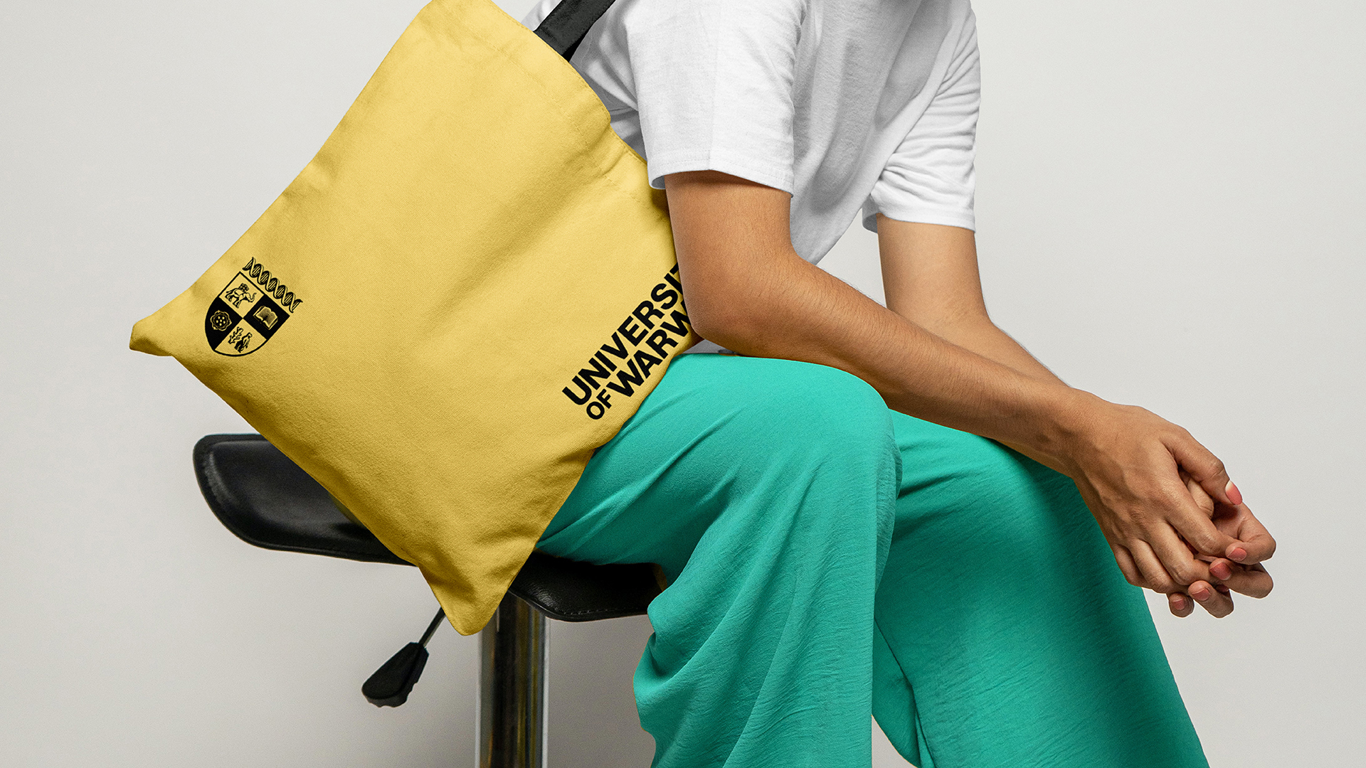 Person sitting in chair with yellow University of Warwick tote bag over shoulder