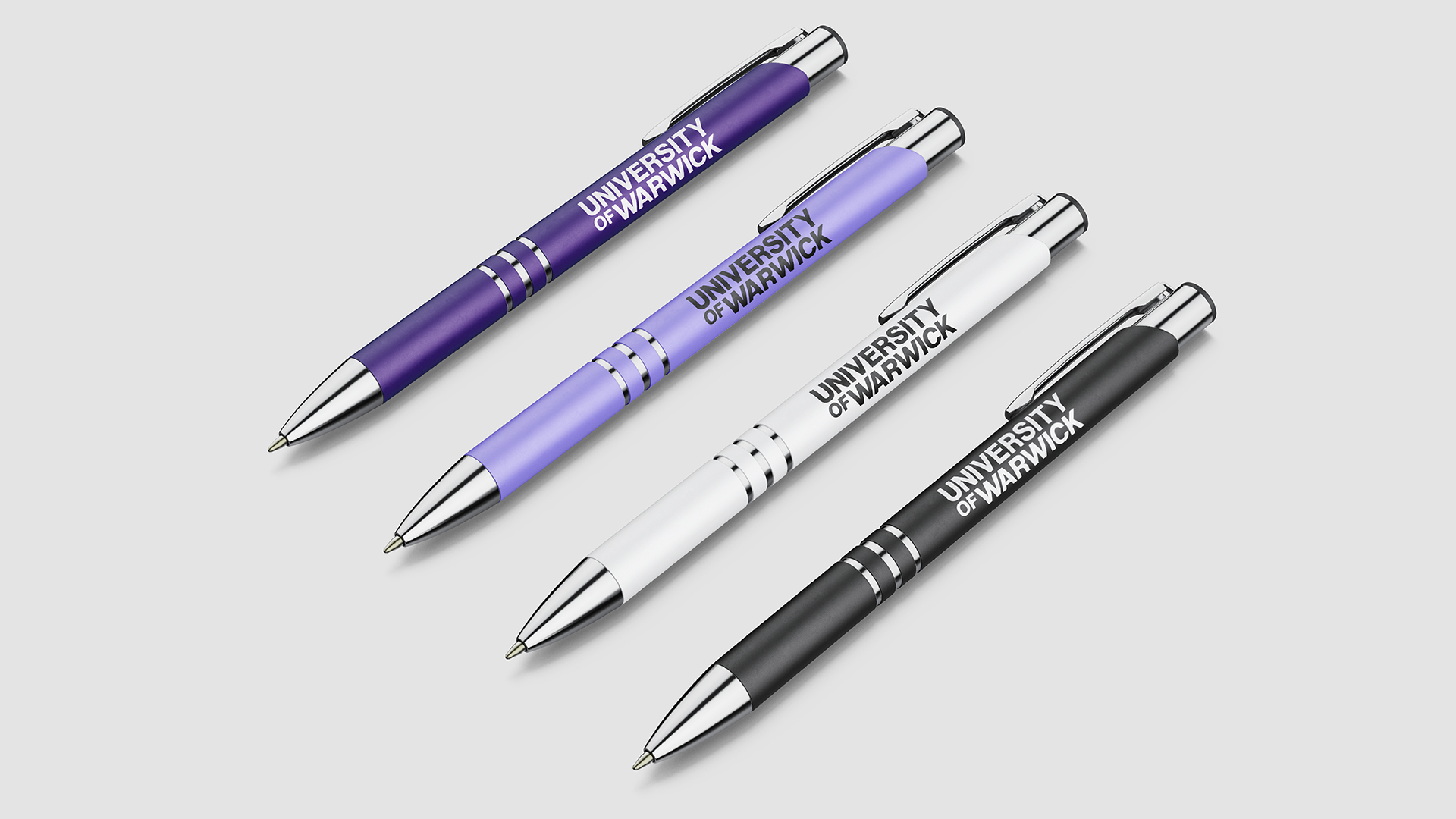 Four pens featuring University of Warwick text on plain grey background