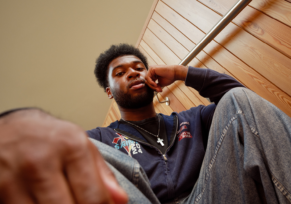 A student seated in the social space at faculty of arts building who is looking down at the camera 