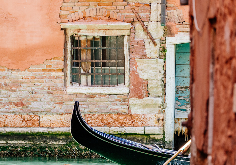 The front of a gondola is seen through a gap between buildings in Venice