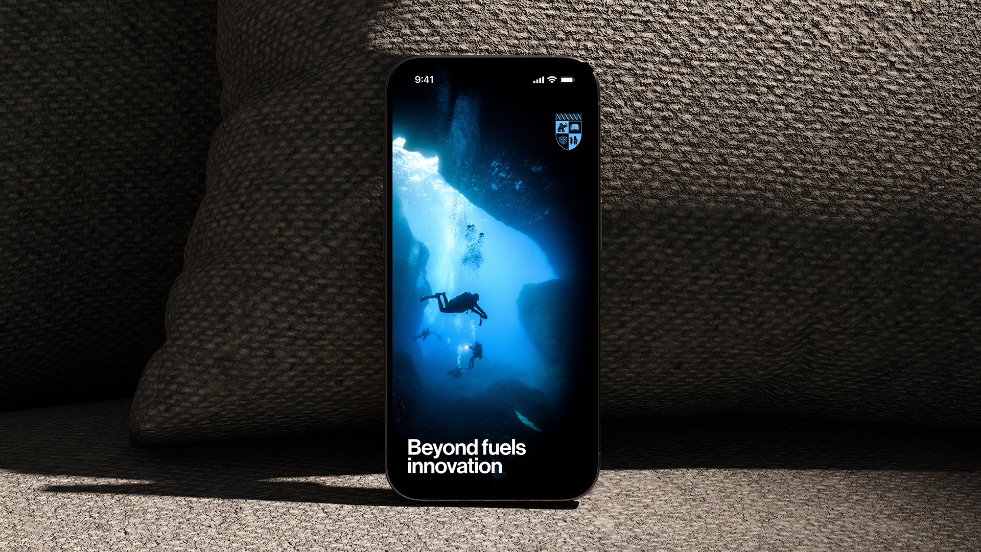 A black smartphone is propped against a stone wall and displays a lock screen image of an underwater cave diver and the text "Beyond fuels innovation"