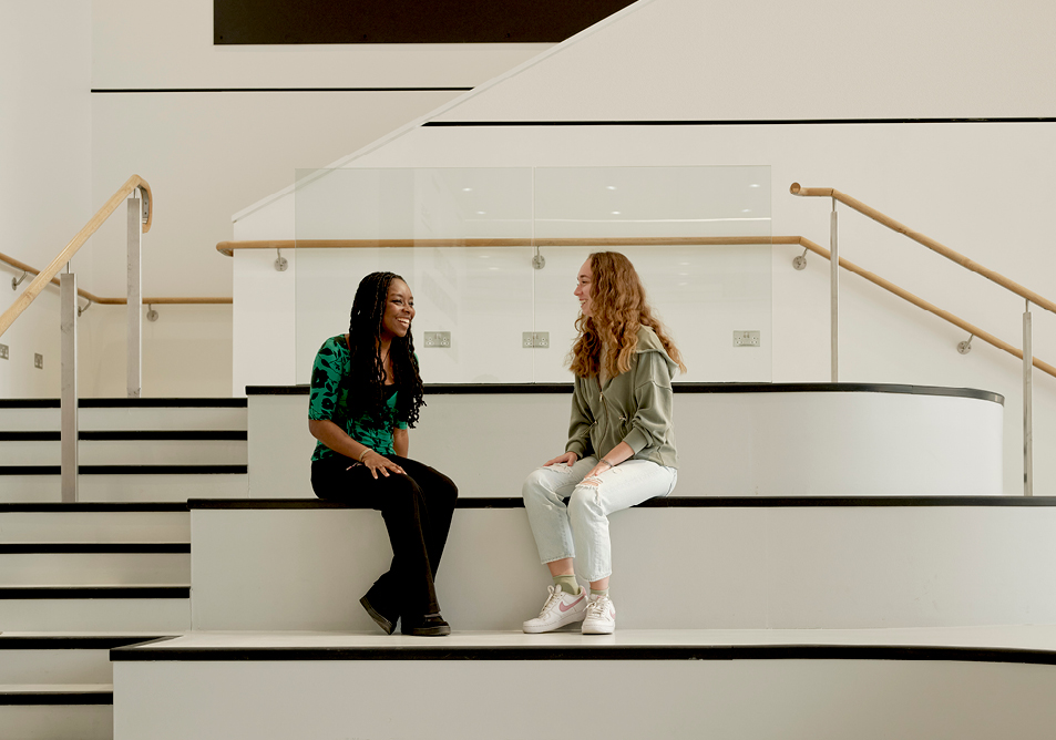 two students sit face to face in conversation on some steps in a social space