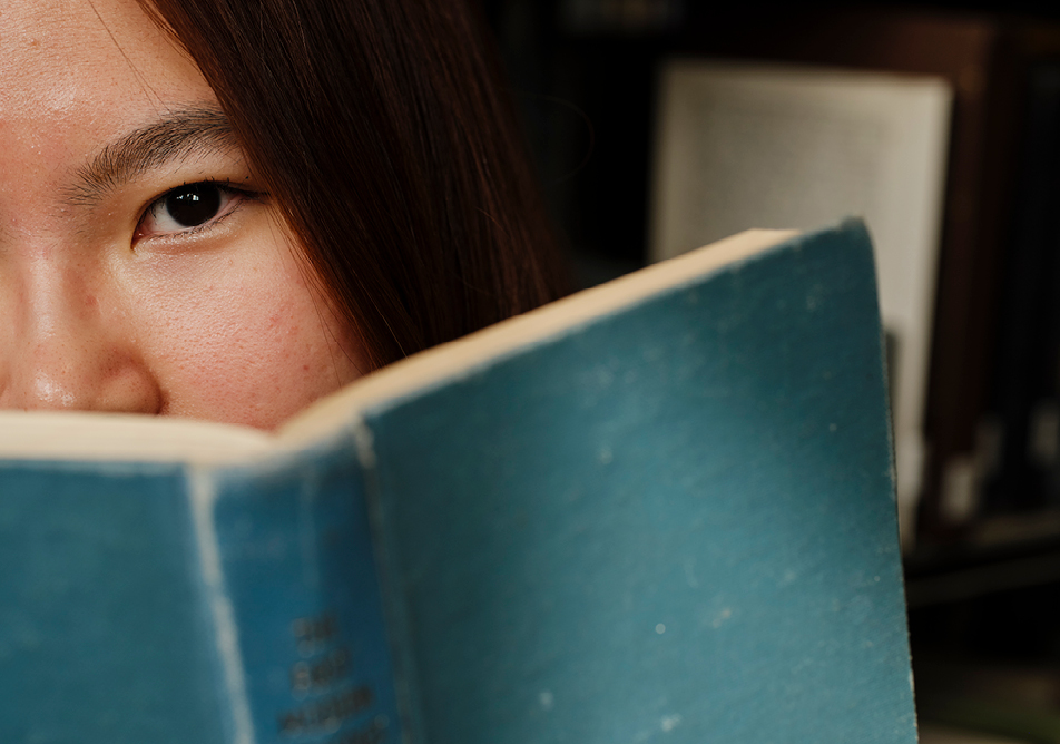 A close up image of part of someone's face peeking out from behind a blue book