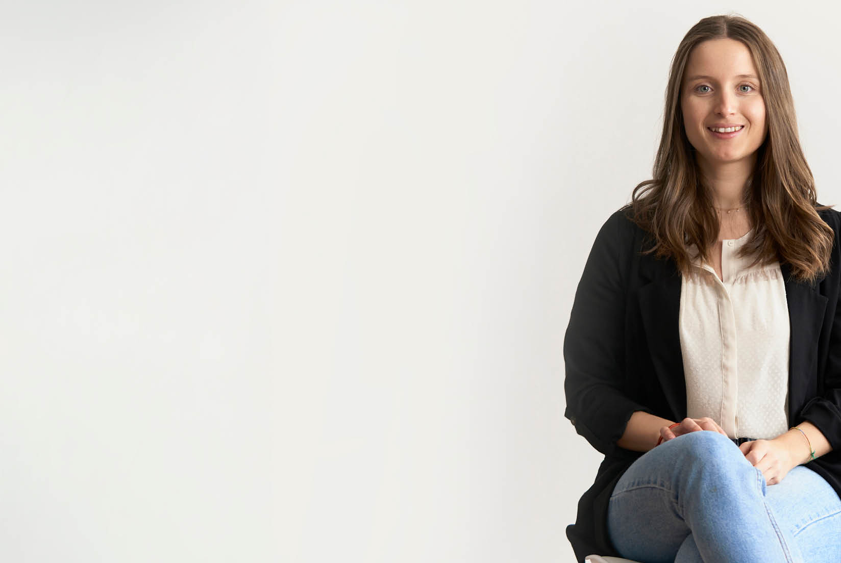 A young girl sitting upright with legs crossed against a white wall in a well-lit room. She is positioned too far to the right in the frame, illustrating poor composition.
