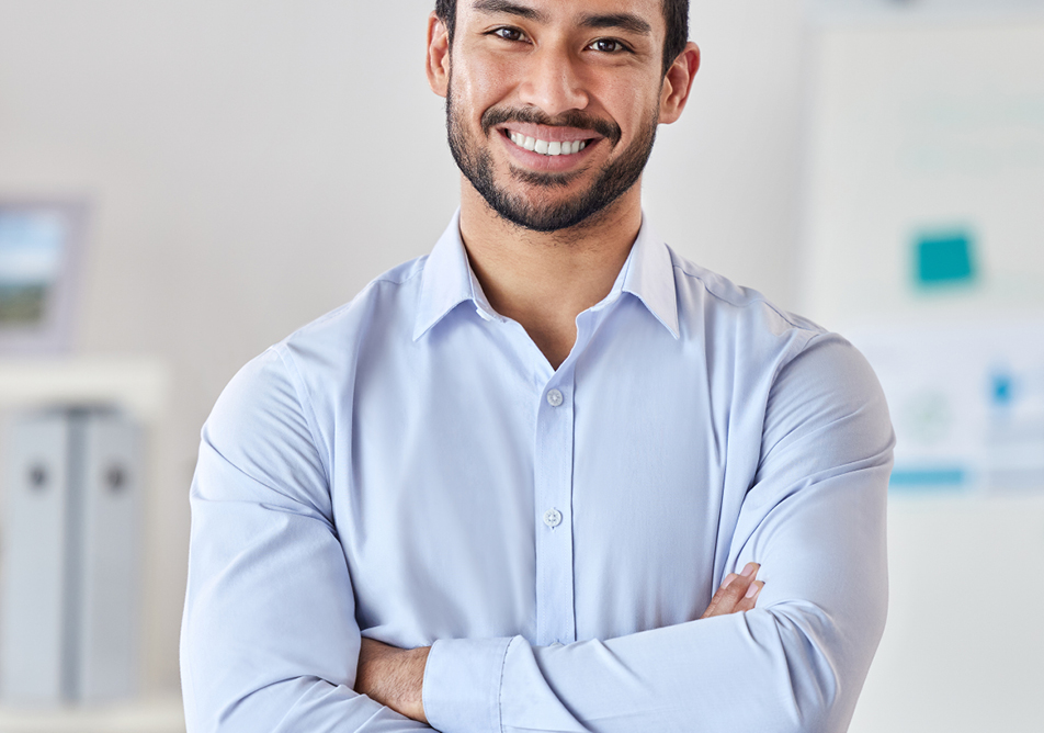A smiling man stands in a lab wearing a pale shirt
