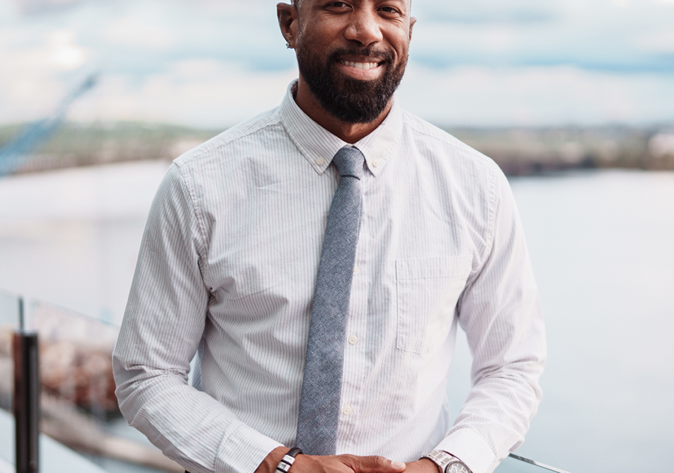 A man in a white shirt and grey tie stands in front of a pale grey landscape