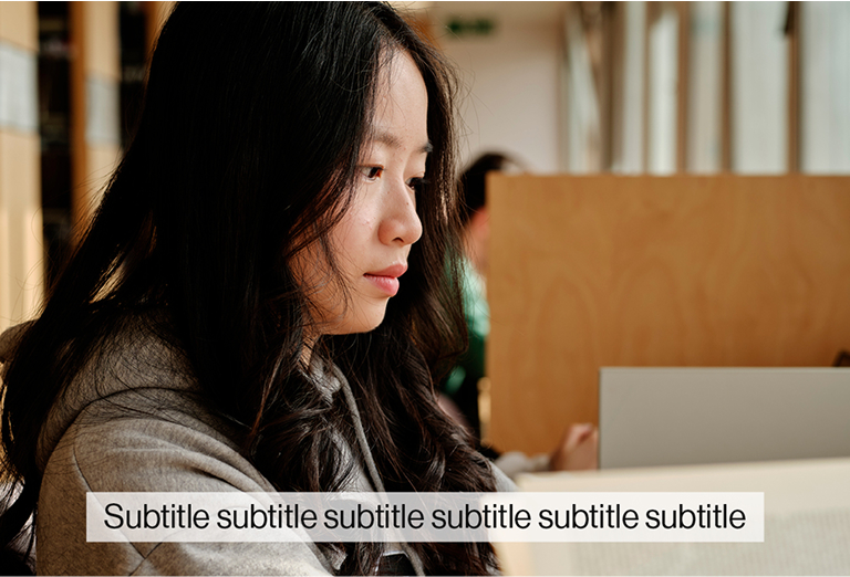 A image of a student at a desk overlayed with black text on a translucent background which says "subtitle, subtitle, subtitle"