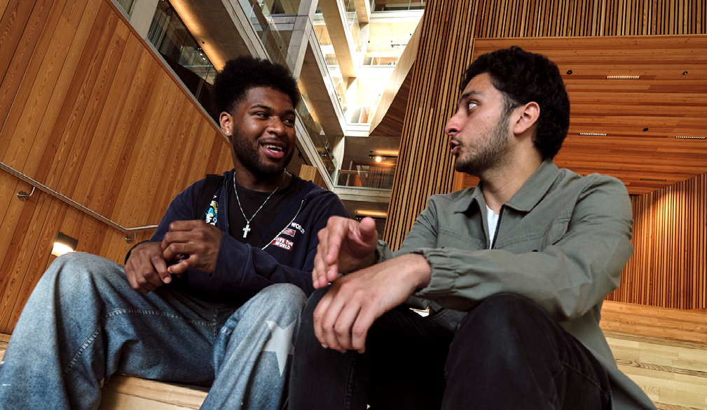 Two young men sitting inside the Faculty of Arts Building (FAB) at the University of Warwick, smiling and chatting with each other.